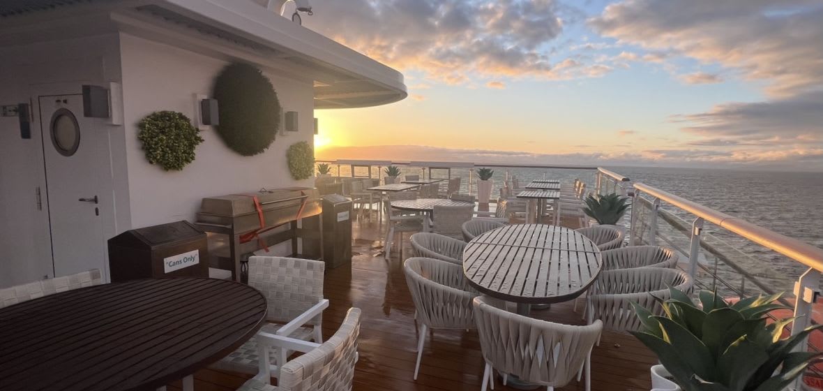 An expansive outdoor lido deck aboard a cruise ship featuring multiple dining tables with white