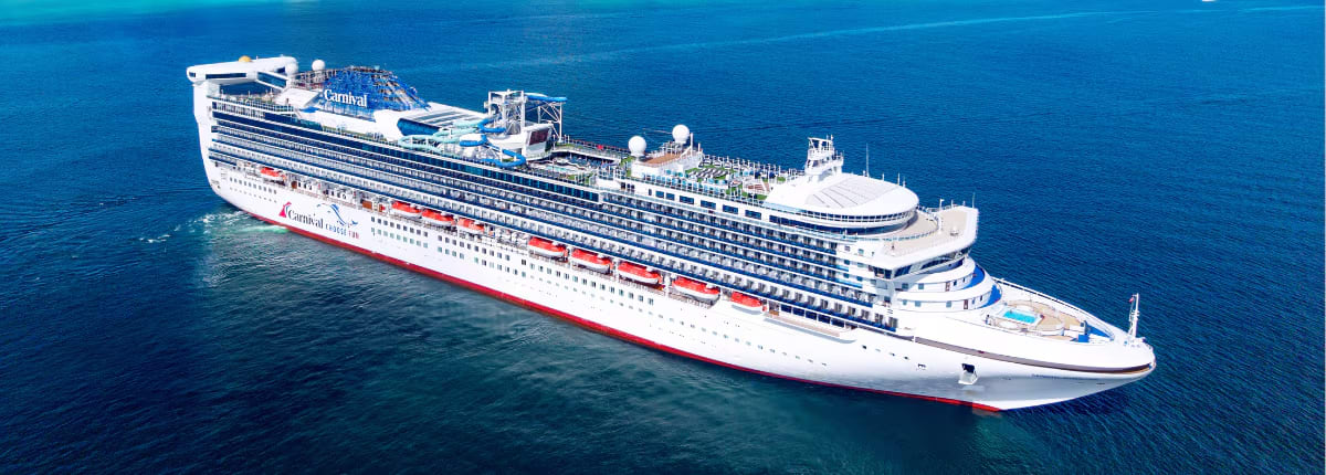 A large modern cruise ship operated by Carnival Cruise Lines sails through deep blue ocean waters