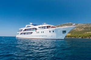 A pristine white motor yacht with multiple decks anchored in crystal-clear turquoise waters near