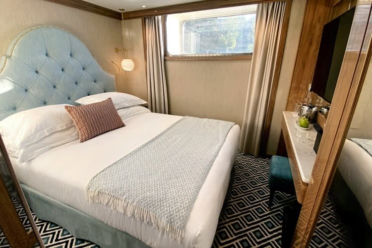 A luxurious stateroom aboard a Uniworld river cruise ship, featuring a plush light blue tufted