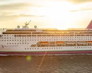 A large modern cruise ship is moored at port during golden hour sunset, displaying