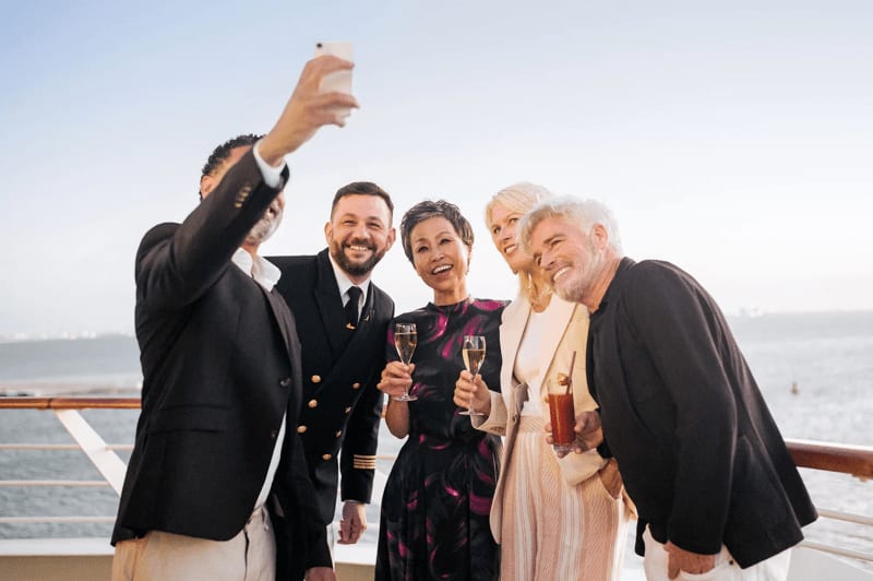 A group of well-dressed passengers and crew members celebrate with champagne glasses on the deck