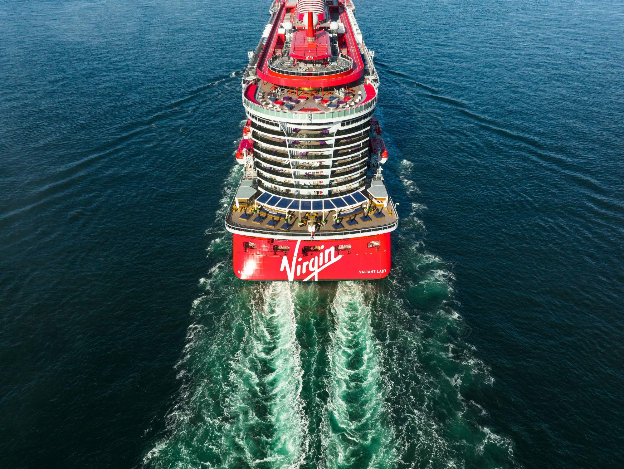 An aerial drone photograph of the Virgin Voyages cruise ship Valiant Lady moving through calm