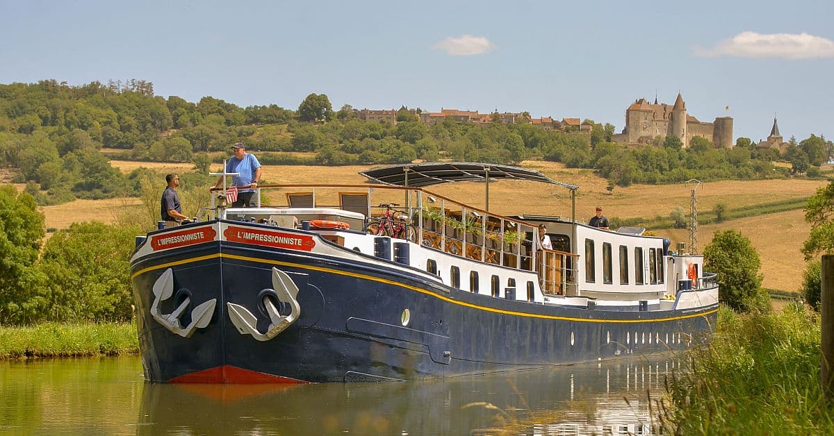 A traditional European river barge named L'Impressionniste navigates a peaceful canal