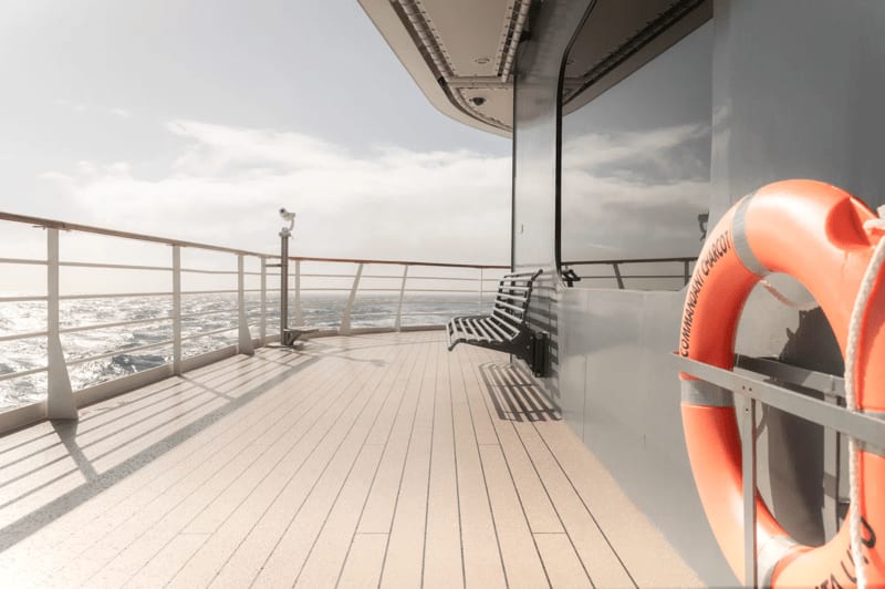 The upper deck of a Ponant expedition cruise vessel overlooking the open ocean, featuring a wooden