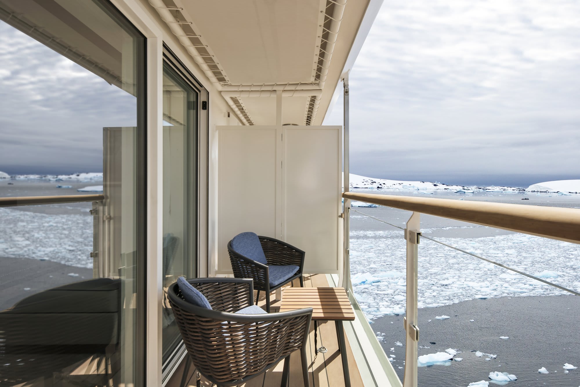 A private balcony on a cruise ship featuring woven chairs overlooking a frozen, ice-filled polar