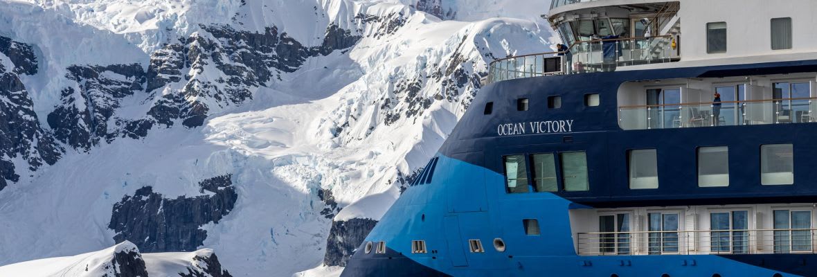 Ocean Victory cruise ship navigating through icy Antarctic waters surrounded by glaciers and snow-covered mountains in Paradise Bay.