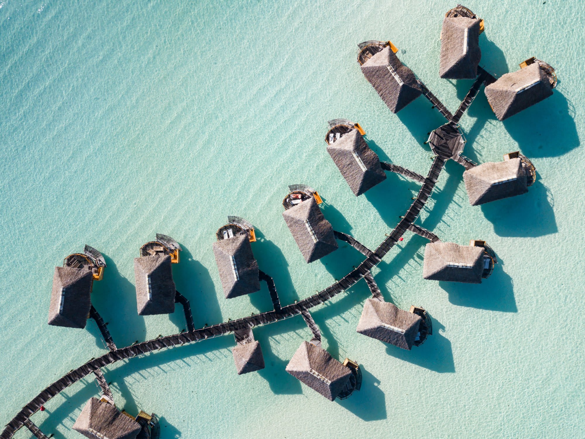 A stunning aerial view of thatched-roof overwater bungalows connected by wooden walkways