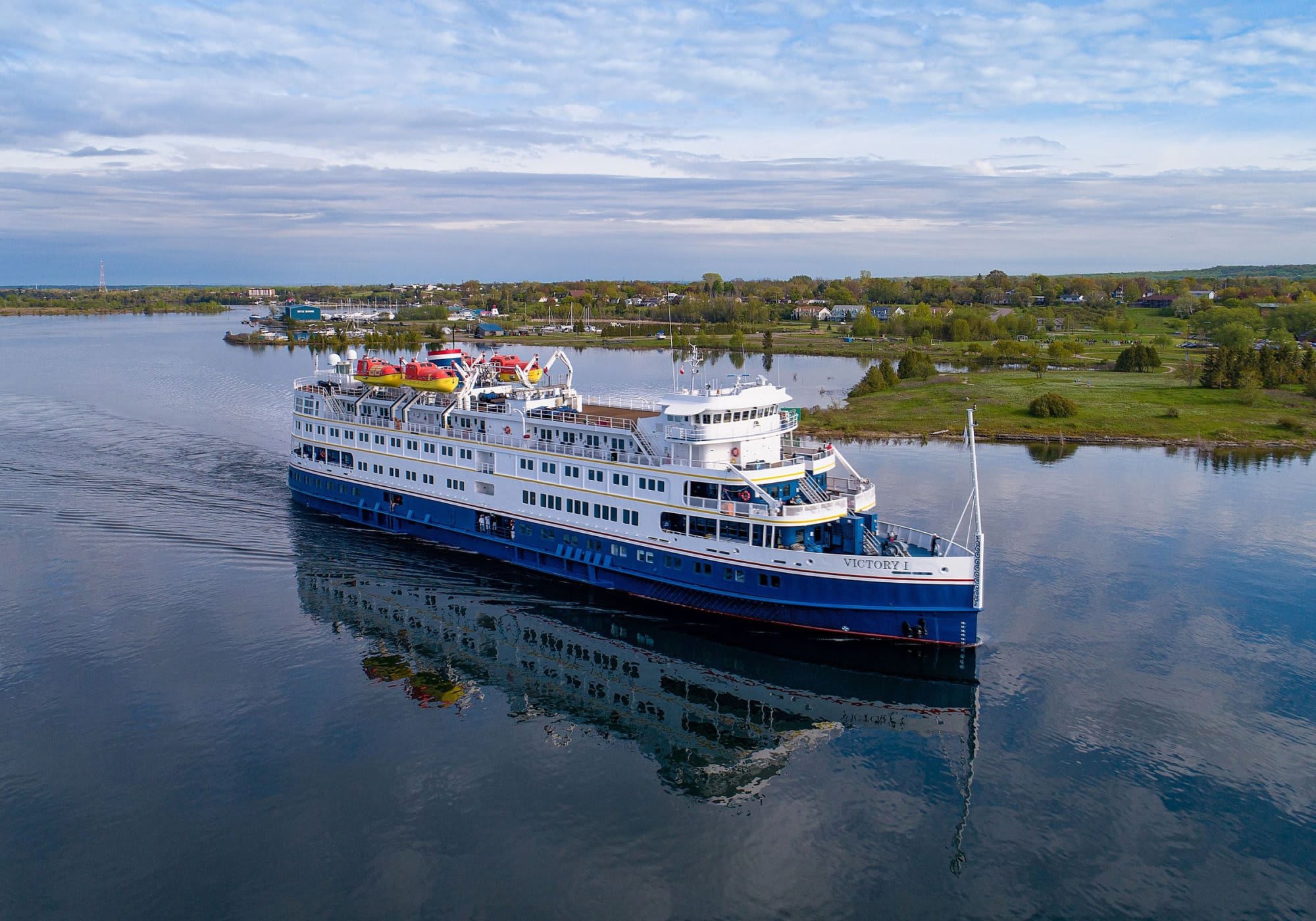 A modern expedition cruise ship, the MS Victory I, anchored in calm blue waters with a picturesque