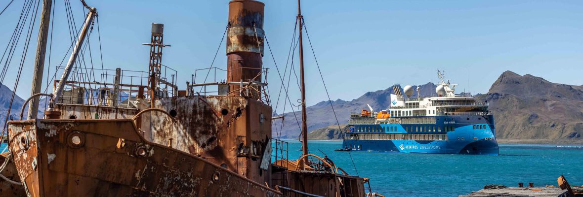 A rusted, abandoned whaling ship sits in the foreground of Grytviken harbor in South Georgia, while