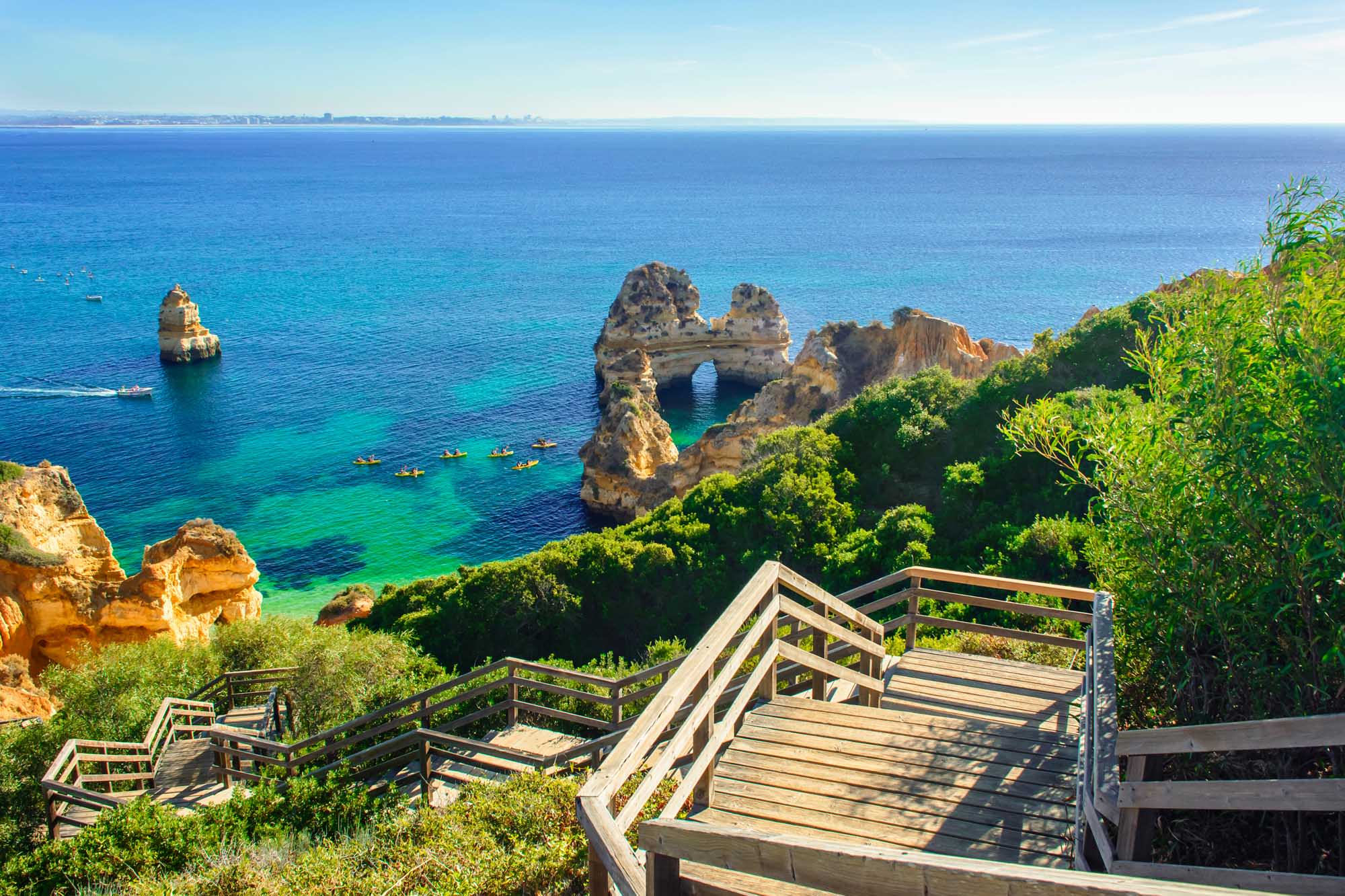 A scenic wooden boardwalk descends toward turquoise waters and dramatic golden rock formations