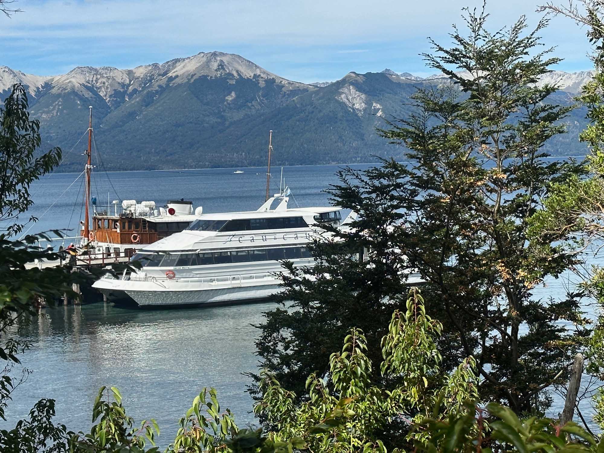 A modern multi-deck cruise vessel and traditional wooden sailing ship are moored in a pristine