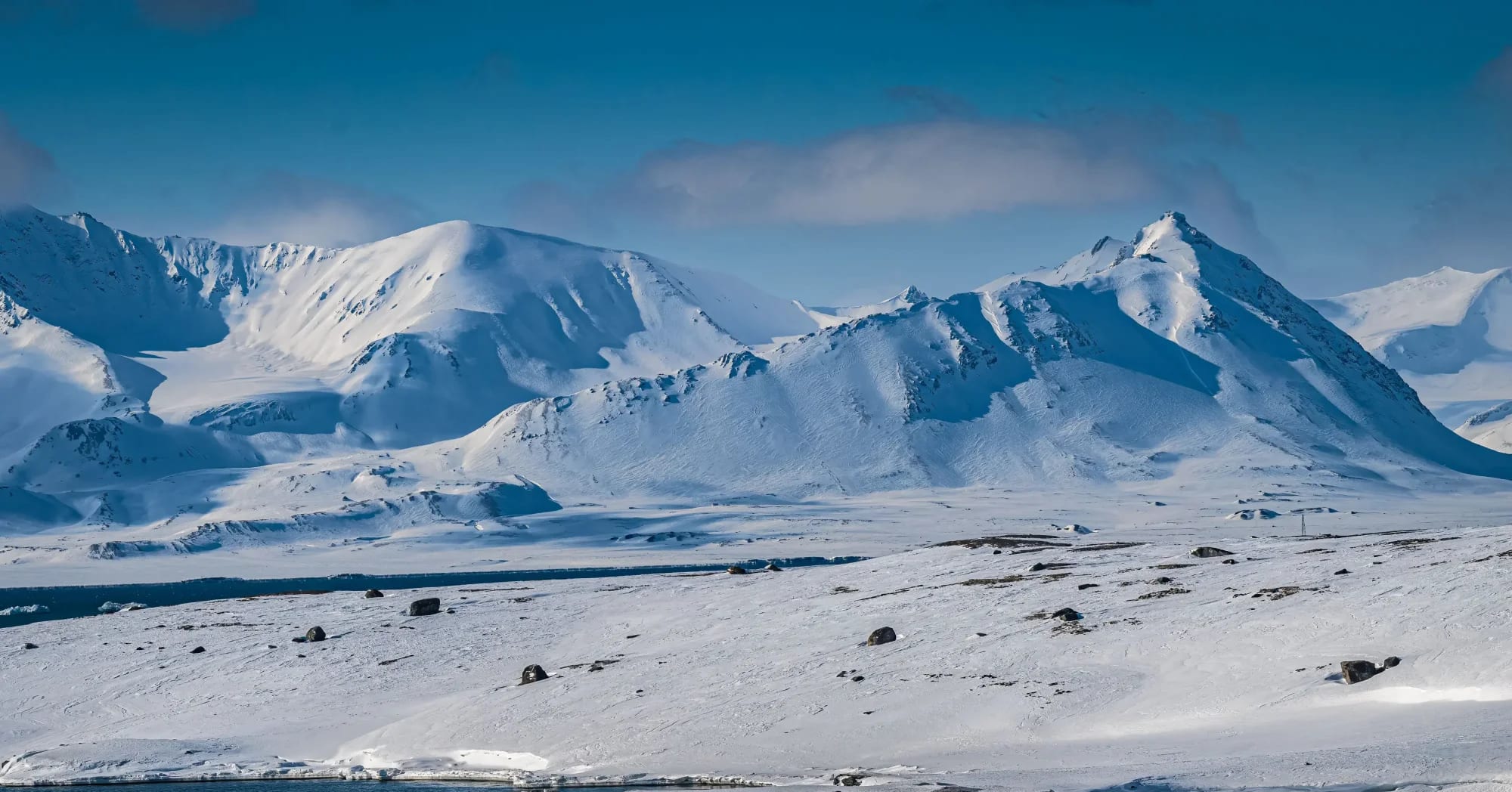A pristine Arctic landscape featuring multiple snow-covered volcanic peaks with distinct conical