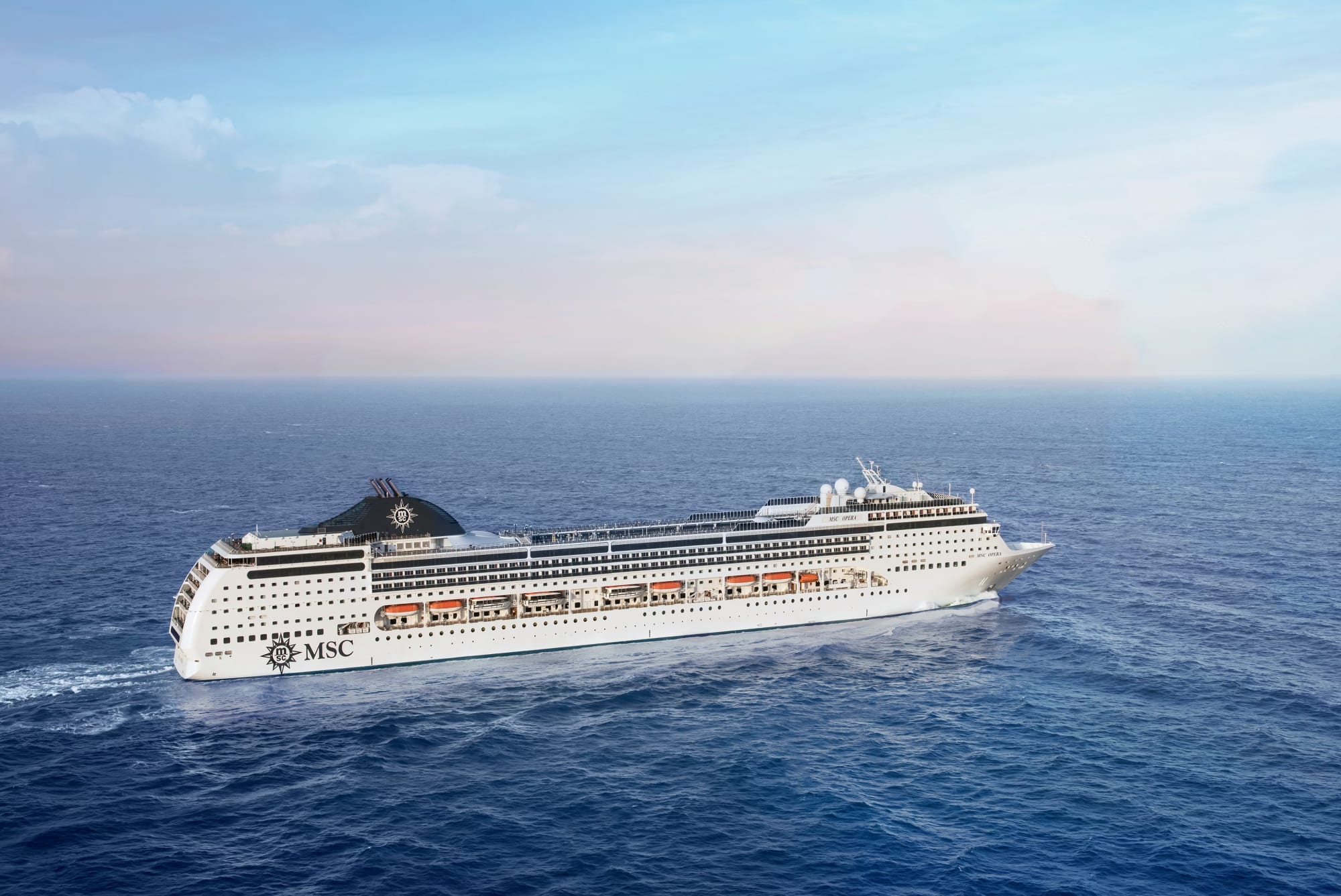 A large modern cruise ship operated by MSC Cruises sails across calm blue waters under a clear sky