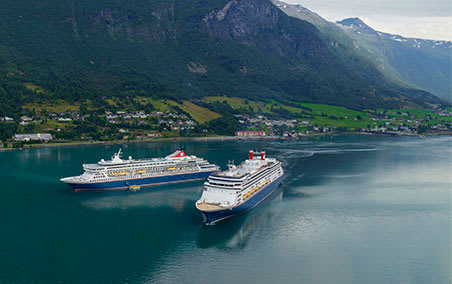 Two large cruise ships are anchored in a pristine turquoise fjord surrounded by dramatic