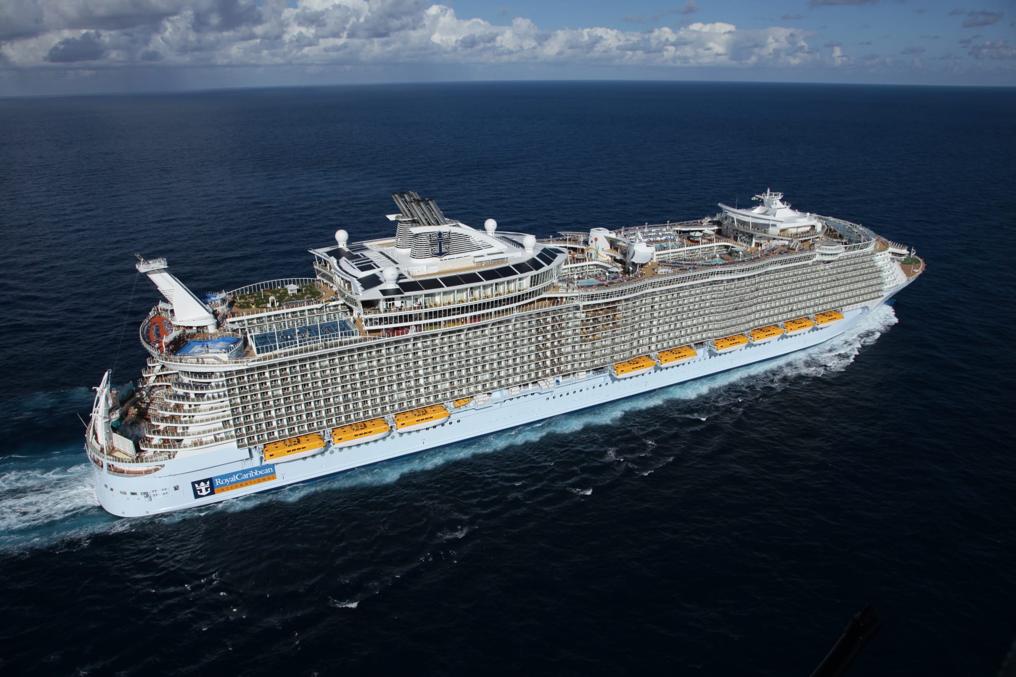 An aerial view of a massive Royal Caribbean cruise ship navigating open ocean waters under partly