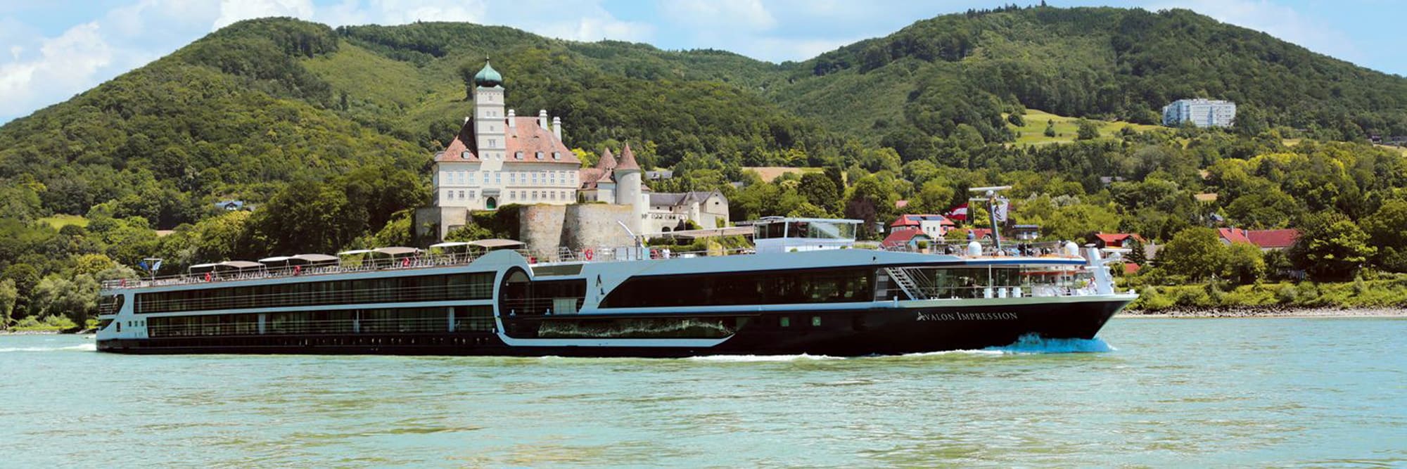 A modern river cruise ship, the Avalon Impression, navigates the Danube River with a picturesque