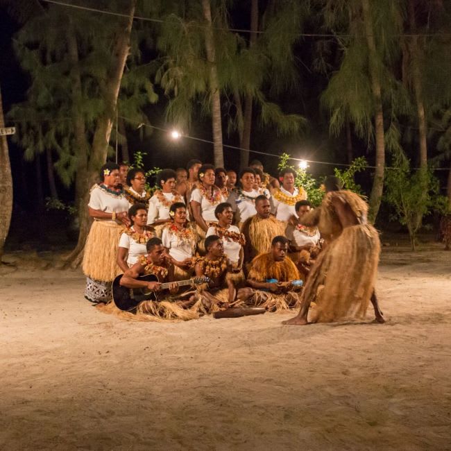 A vibrant nighttime cultural gathering on a sandy beach featuring a large group of performers