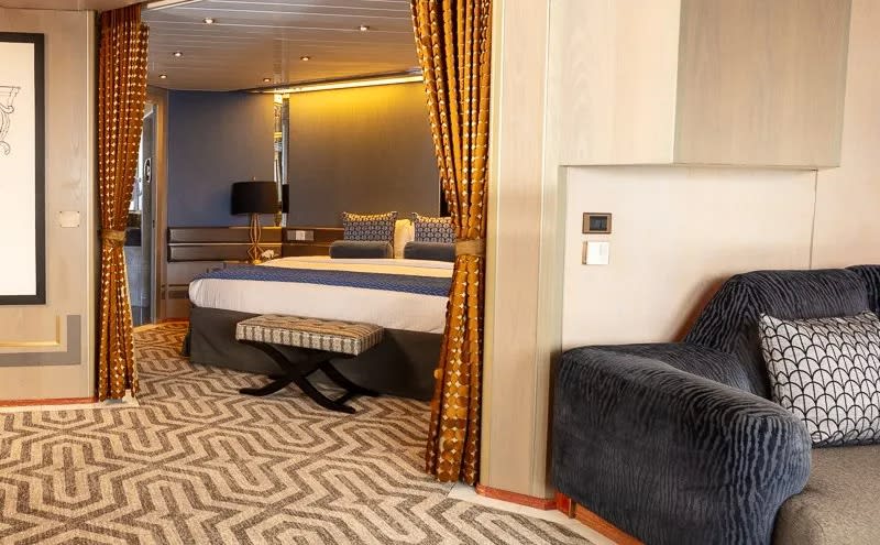 A modern cruise ship cabin featuring a separate sleeping alcove with a queen-sized bed