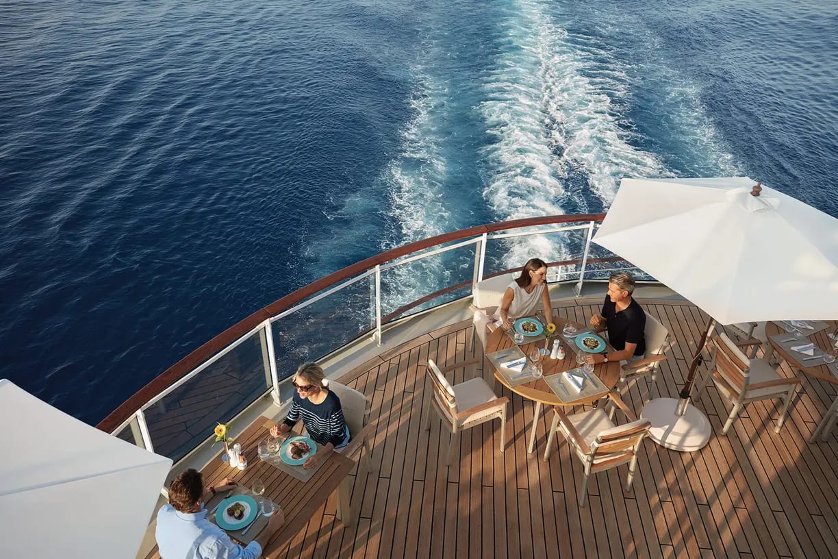 Passengers enjoy an upscale outdoor dining experience on a cruise ship's aft deck, with elegant