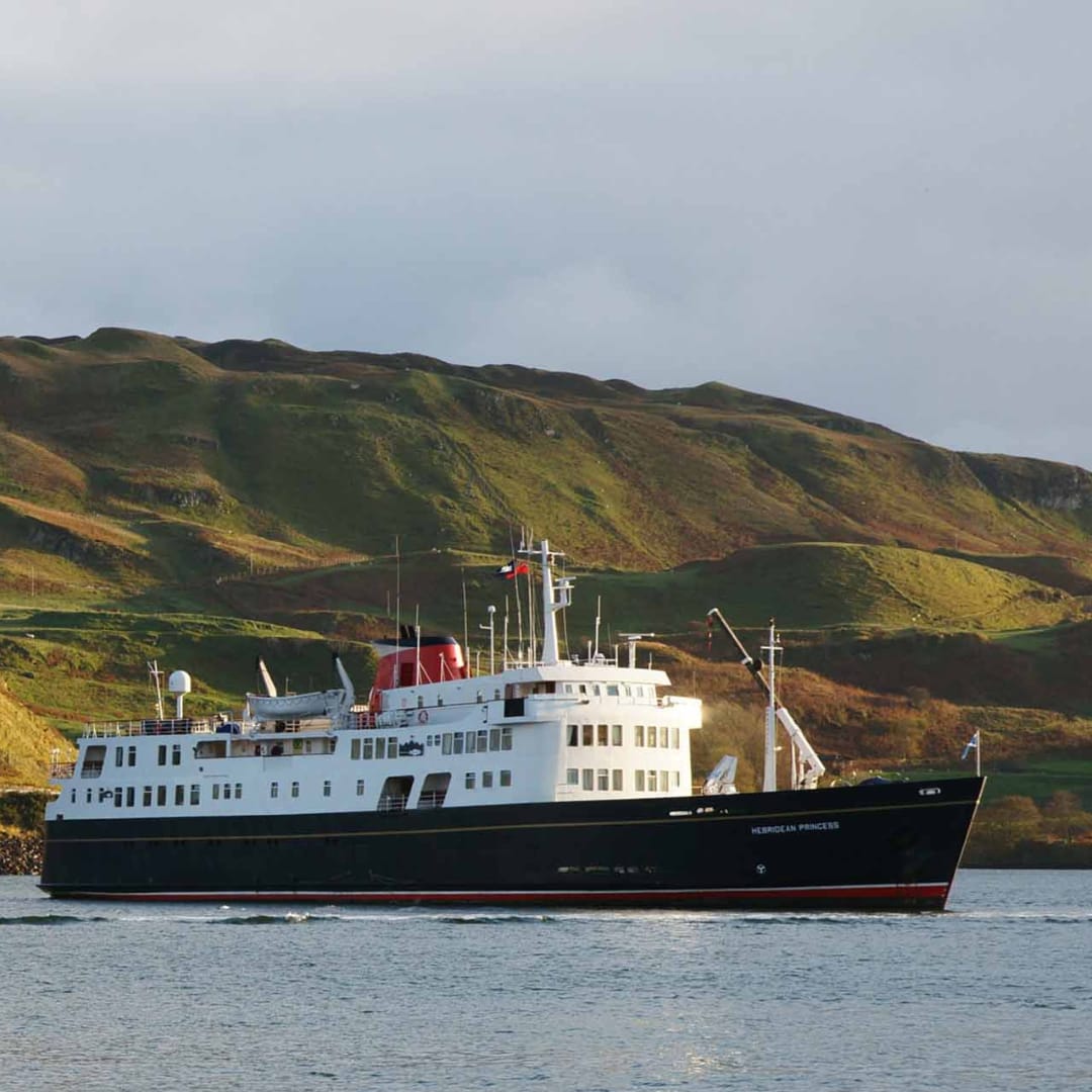 The Hebridean Princess, a small luxury expedition cruise ship, anchors in calm waters with dramatic
