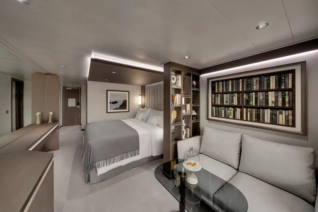 A sophisticated, modern luxury cruise ship suite featuring a king bed with crisp white linens