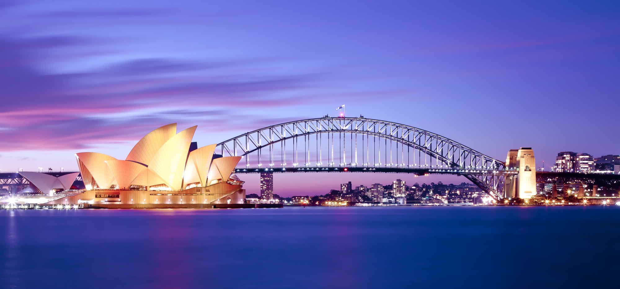 An iconic twilight photograph of Sydney's most famous landmarks, featuring the illuminated Sydney