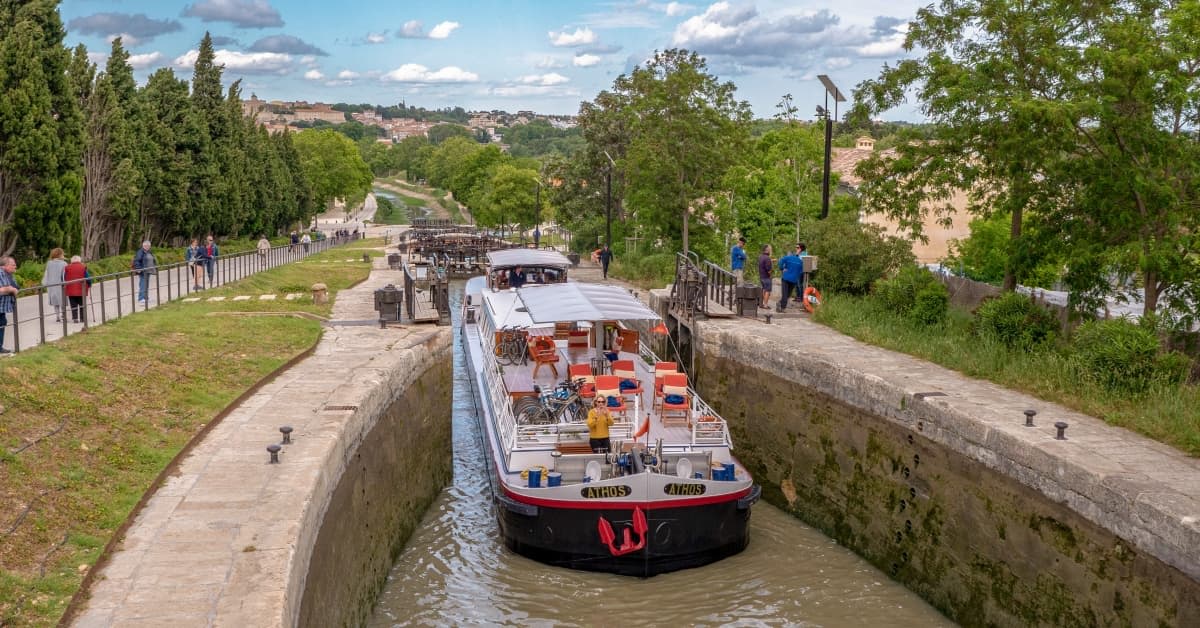 A red and white river cruise barge navigates through a stone lock system on a European waterway