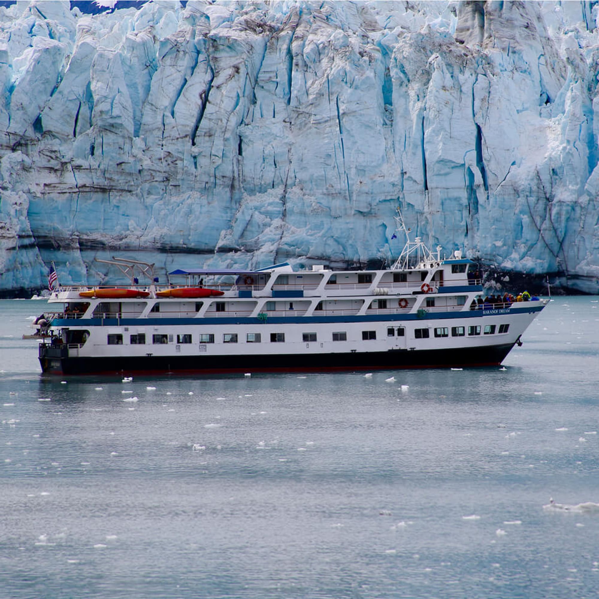 A large multi-deck cruise ship anchored in pristine glacial waters, with a massive blue glacier