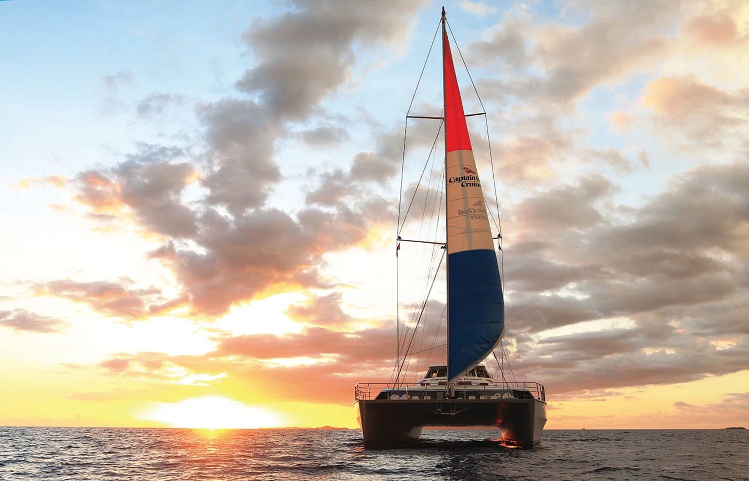 A modern catamaran with a red and white sail displaying 'Captain Cruse' branding sails gracefully