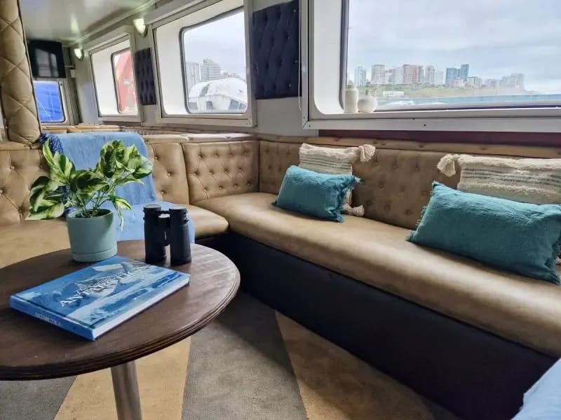An elegant interior lounge aboard a luxury yacht or expedition vessel, featuring beige tufted