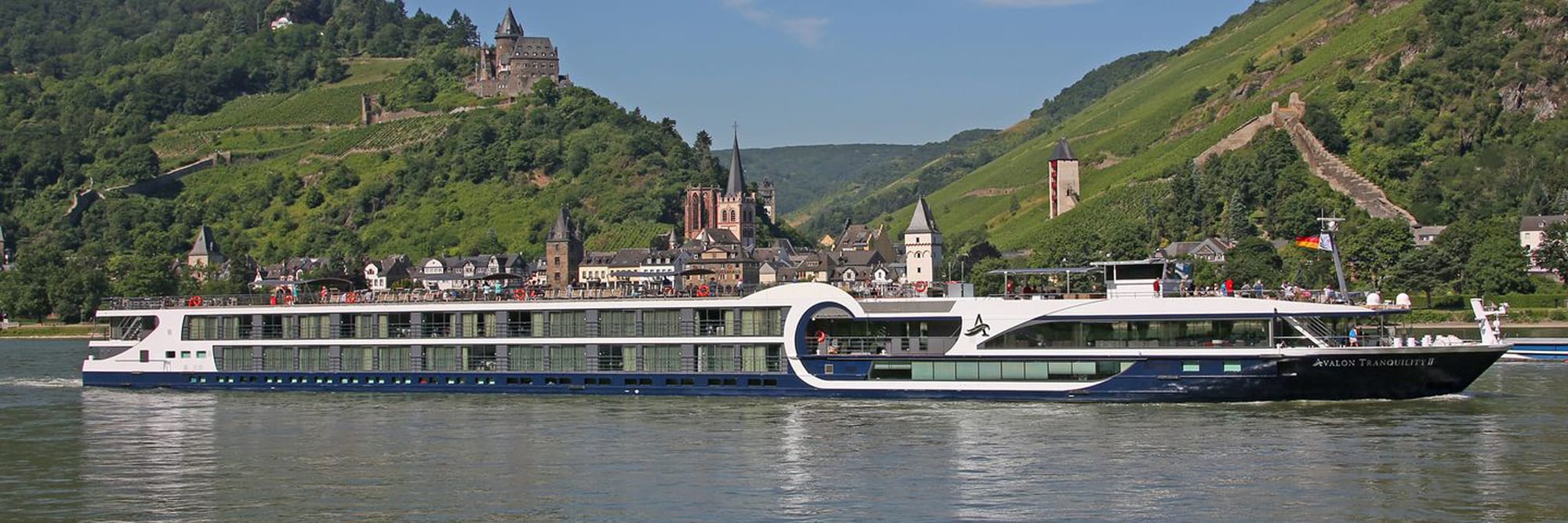 A modern river cruise ship, the Avalon Tranquility II, sails along the Rhine River with