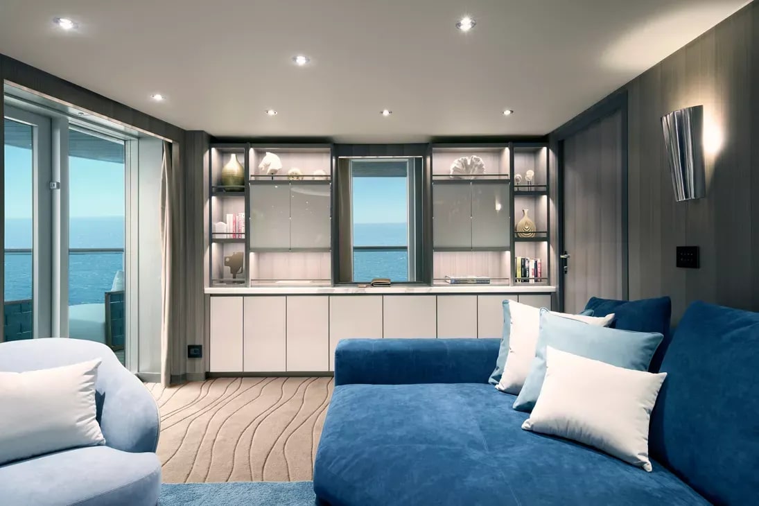 A modern luxury cruise ship suite featuring a king-size bed with blue upholstery, floor-to-ceiling
