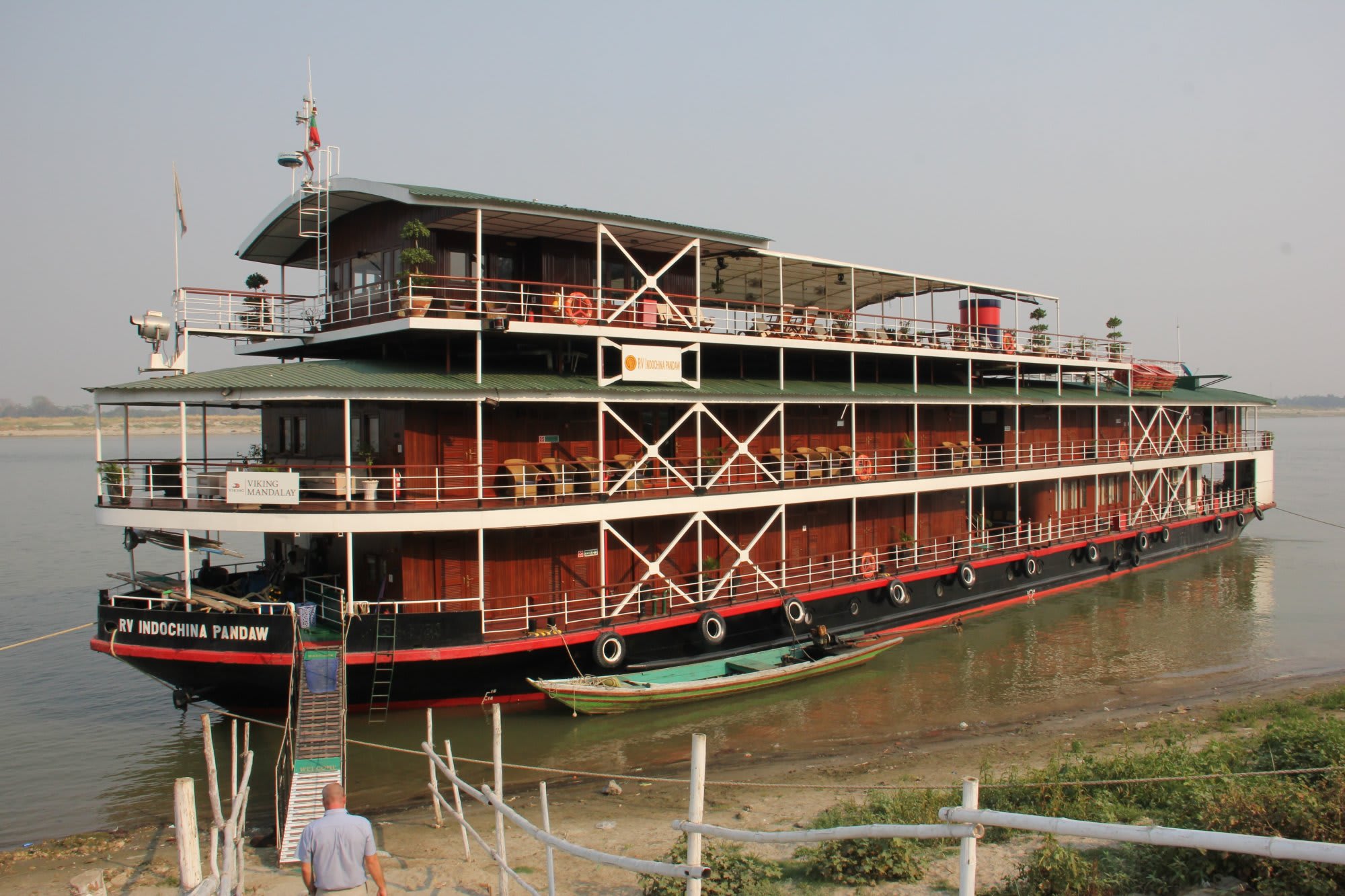A striking three-deck river cruise vessel named RV Indochina Pandaw docked along a riverbank