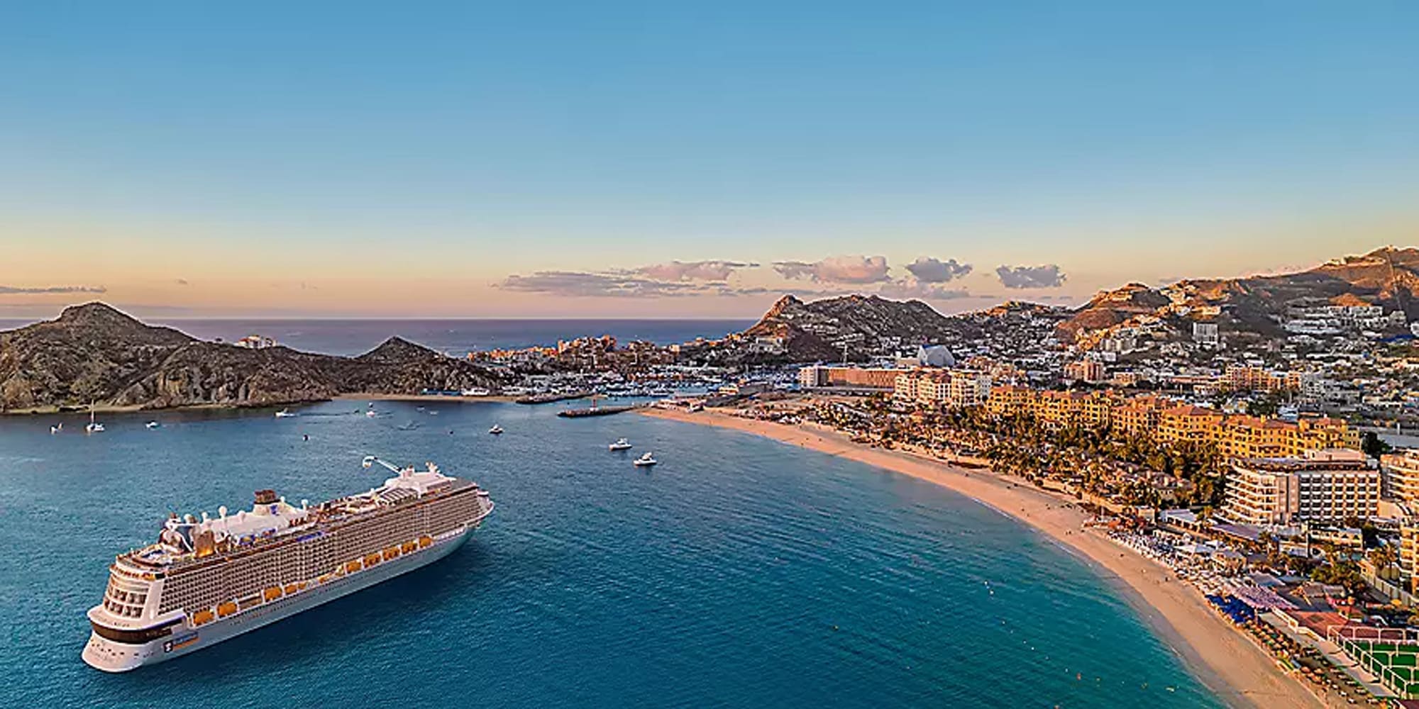 A large modern cruise ship anchors in the turquoise waters of Cabo San Lucas, with the iconic rocky