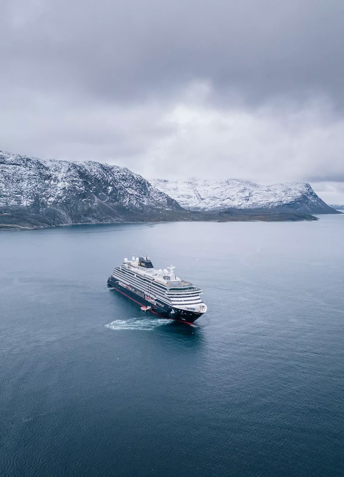 A modern luxury expedition cruise ship navigates the icy waters of Greenland, with snow-capped