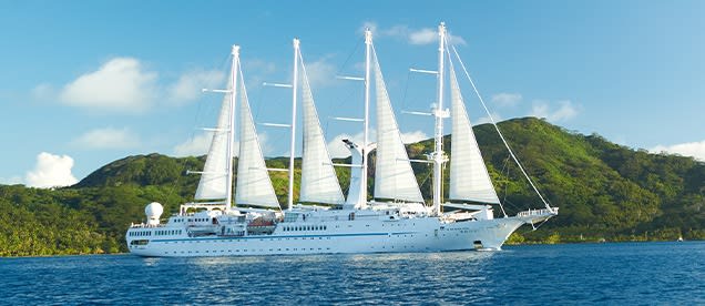 A luxurious white sailing yacht with four full masts under full sail on turquoise tropical waters