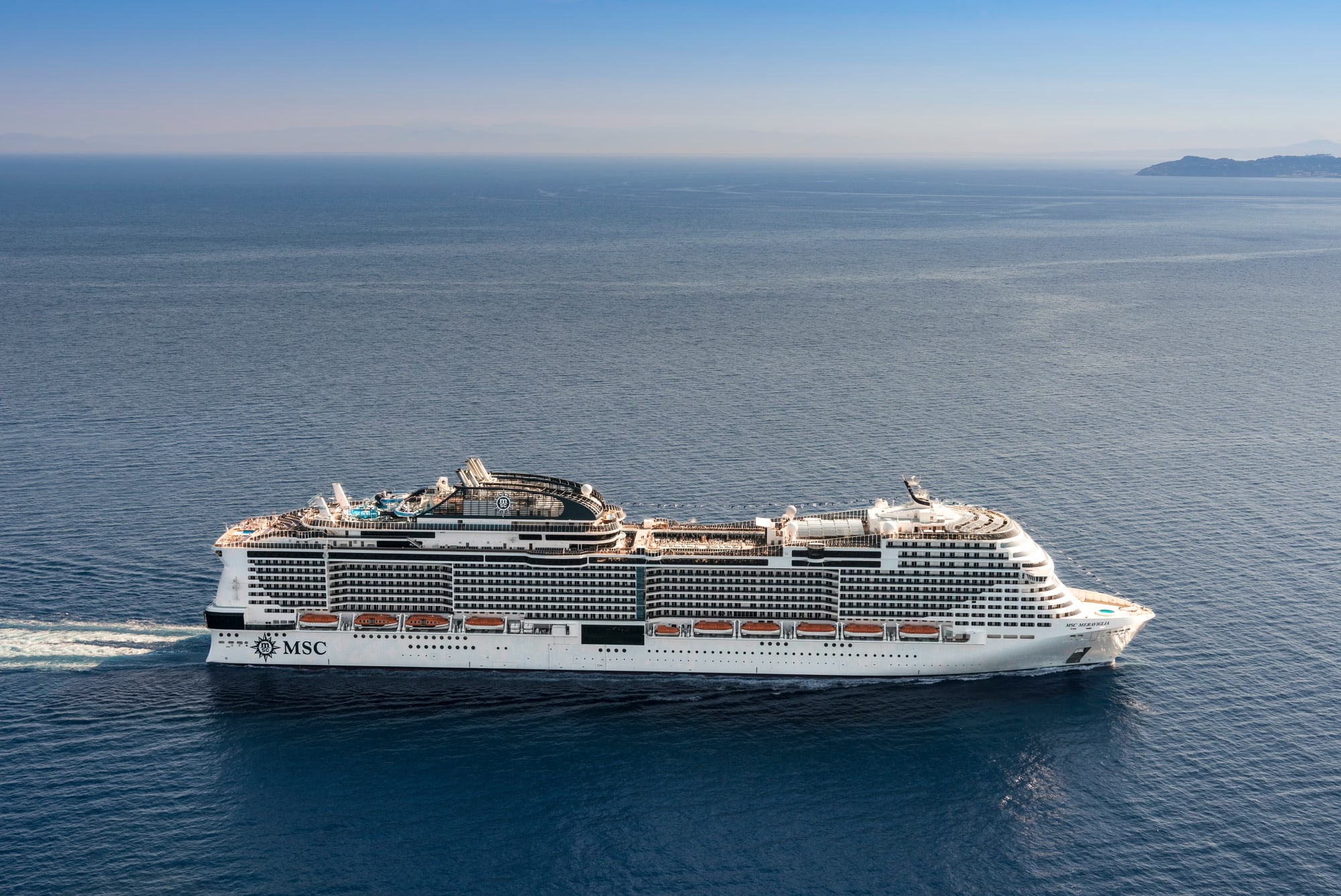 A large modern cruise ship operated by MSC Cruises sailing through calm blue waters. The white