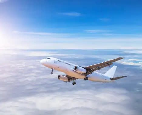 A white commercial passenger aircraft is captured in flight against a brilliant blue sky, cruising