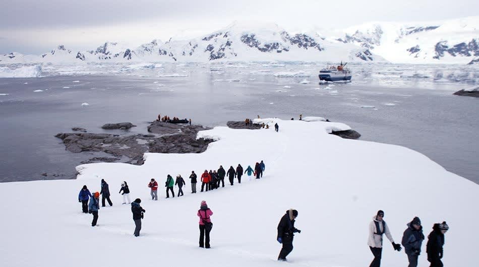 A group of expedition tourists in colorful cold-weather gear walk across snow-covered ice floes