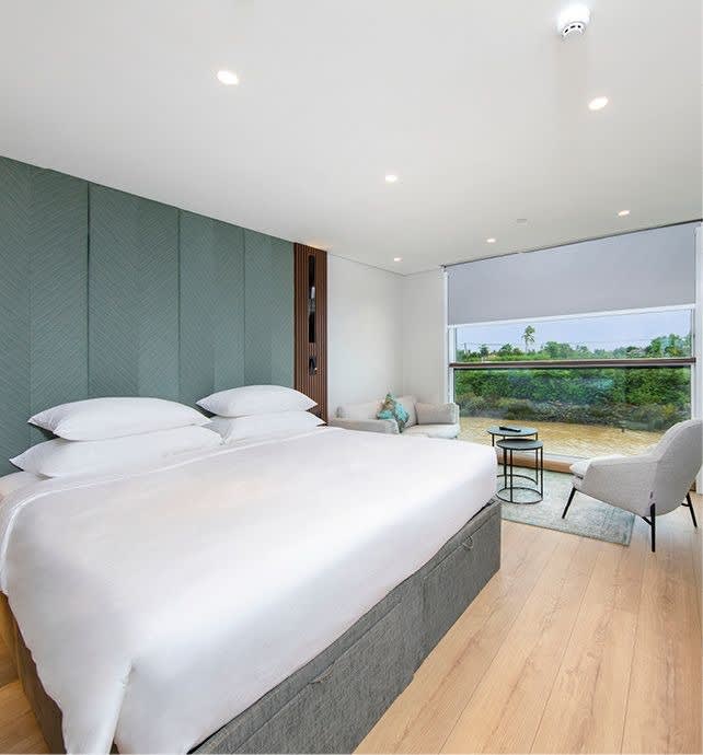 A modern, spacious suite featuring a king-size bed with white linens, a teal-green quilted