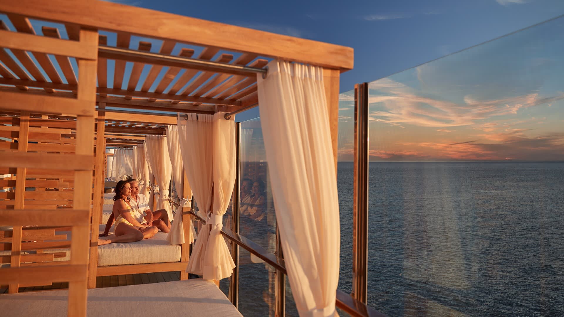 An elegant outdoor cabana area featuring wooden pergolas with flowing cream-colored curtains