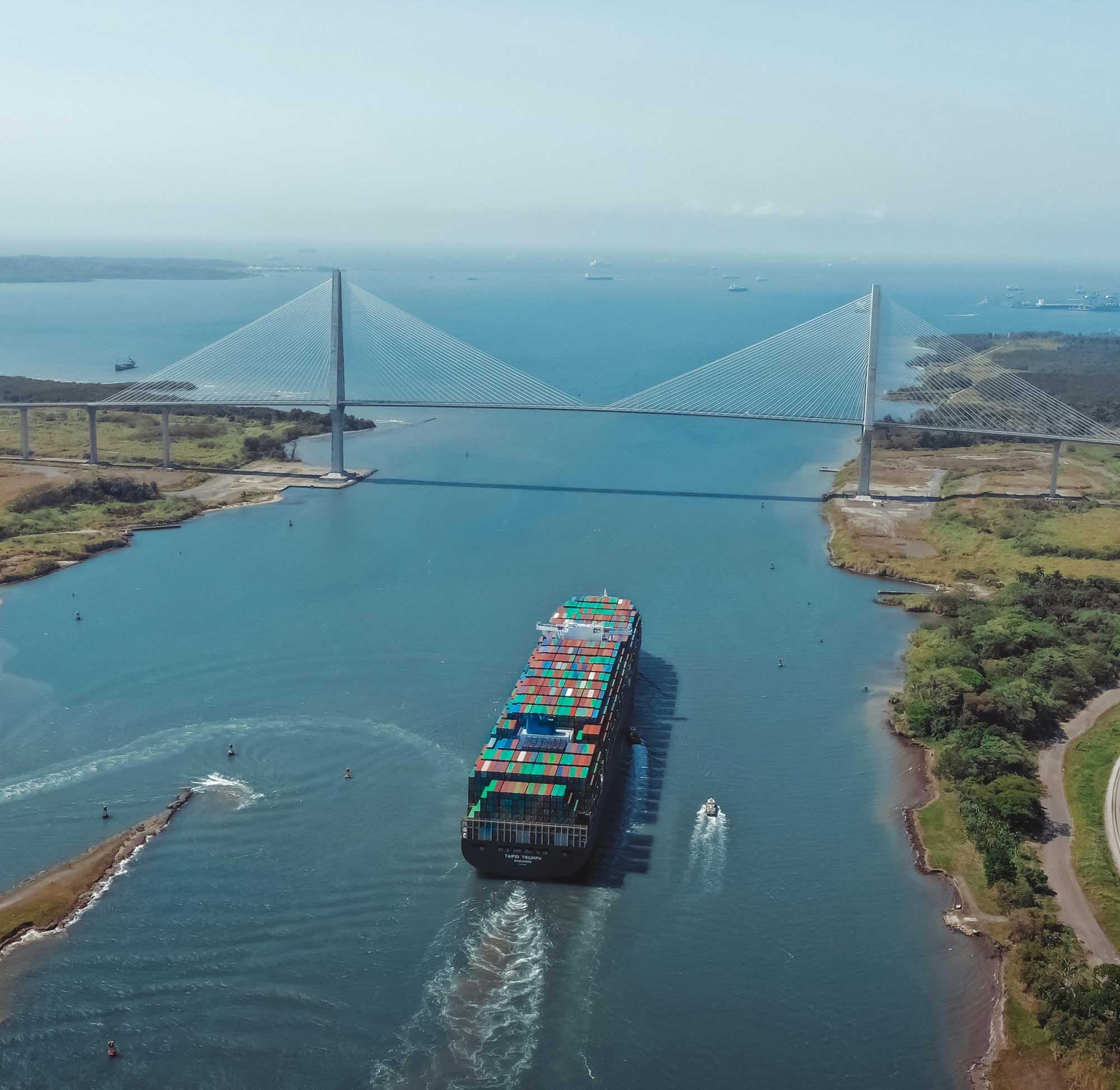 A large container ship laden with colorful cargo containers navigates through the Panama Canal