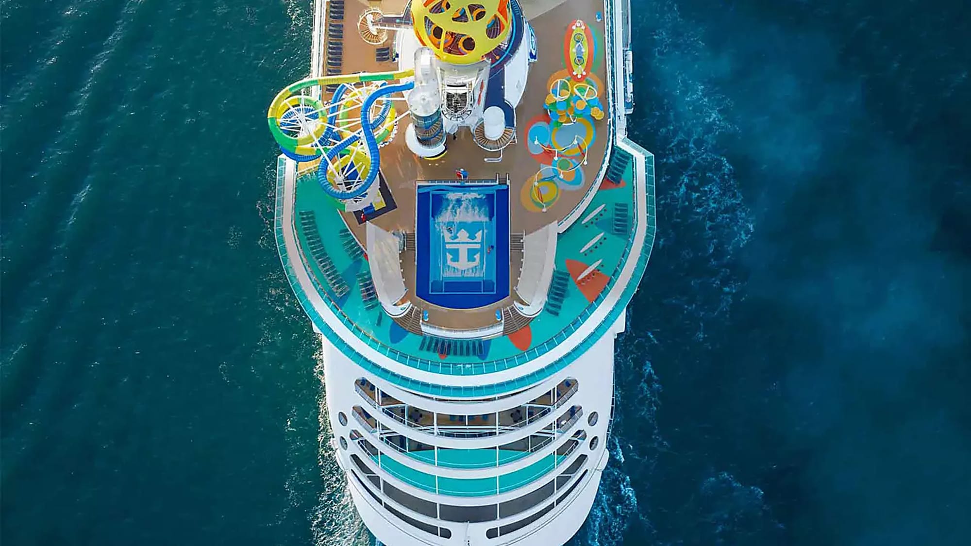 An overhead aerial view of a large cruise ship's upper deck featuring vibrant water slides
