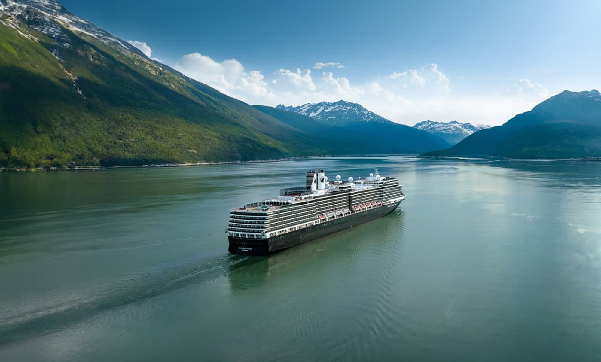A modern Holland America Line cruise ship navigates through pristine glacial waters surrounded