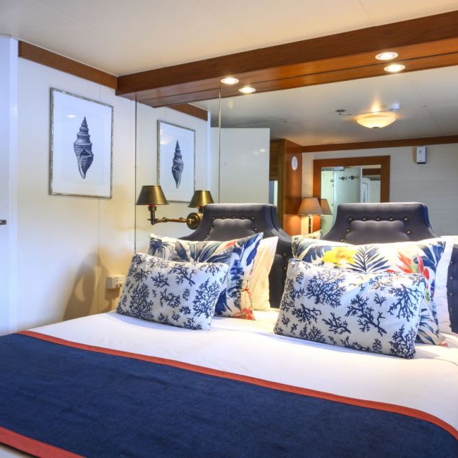 An elegantly designed cruise ship cabin featuring dual beds with navy upholstered headboards