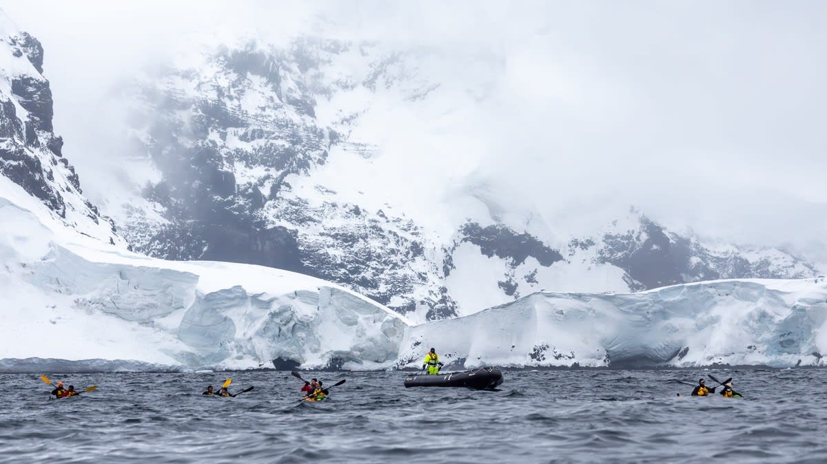 Adventure travelers in inflatable Zodiac boats explore the pristine Antarctic landscape, navigating