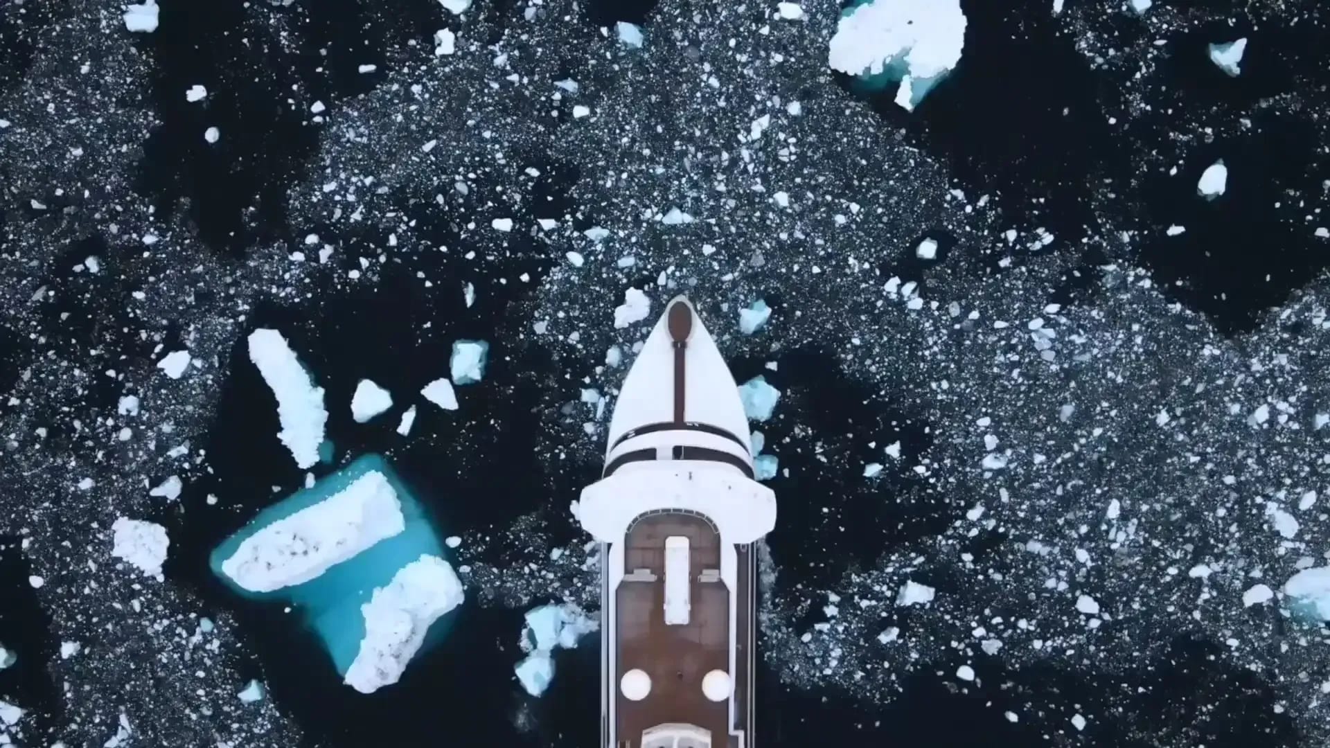 An overhead aerial view of a small expedition cruise ship navigating through Arctic pack ice
