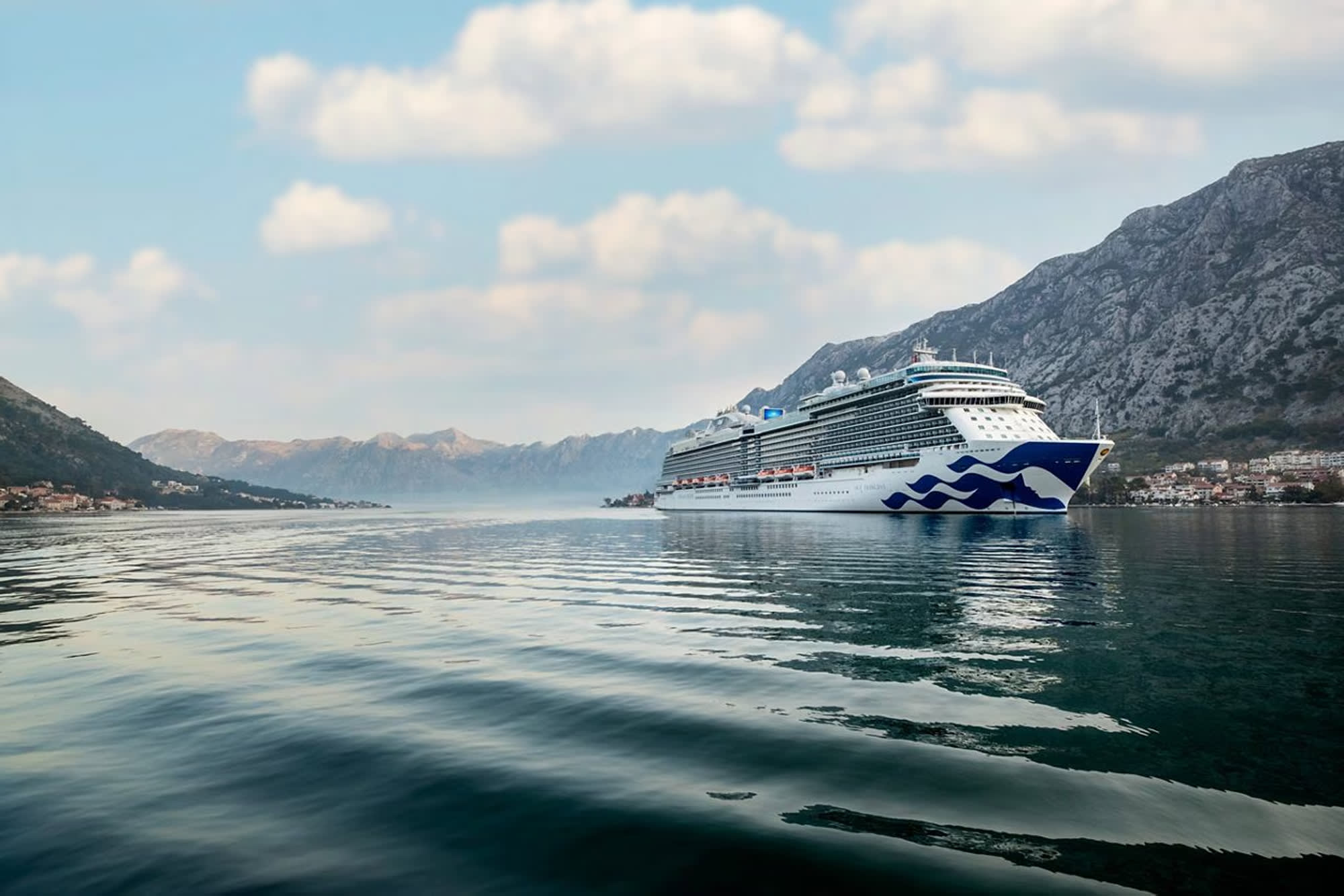 A large modern cruise ship sailing through a picturesque mountain landscape with rocky peaks