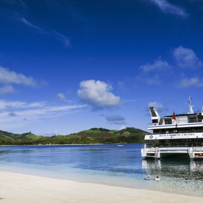 A Holland America Line cruise ship is docked at a pristine tropical beach with turquoise waters